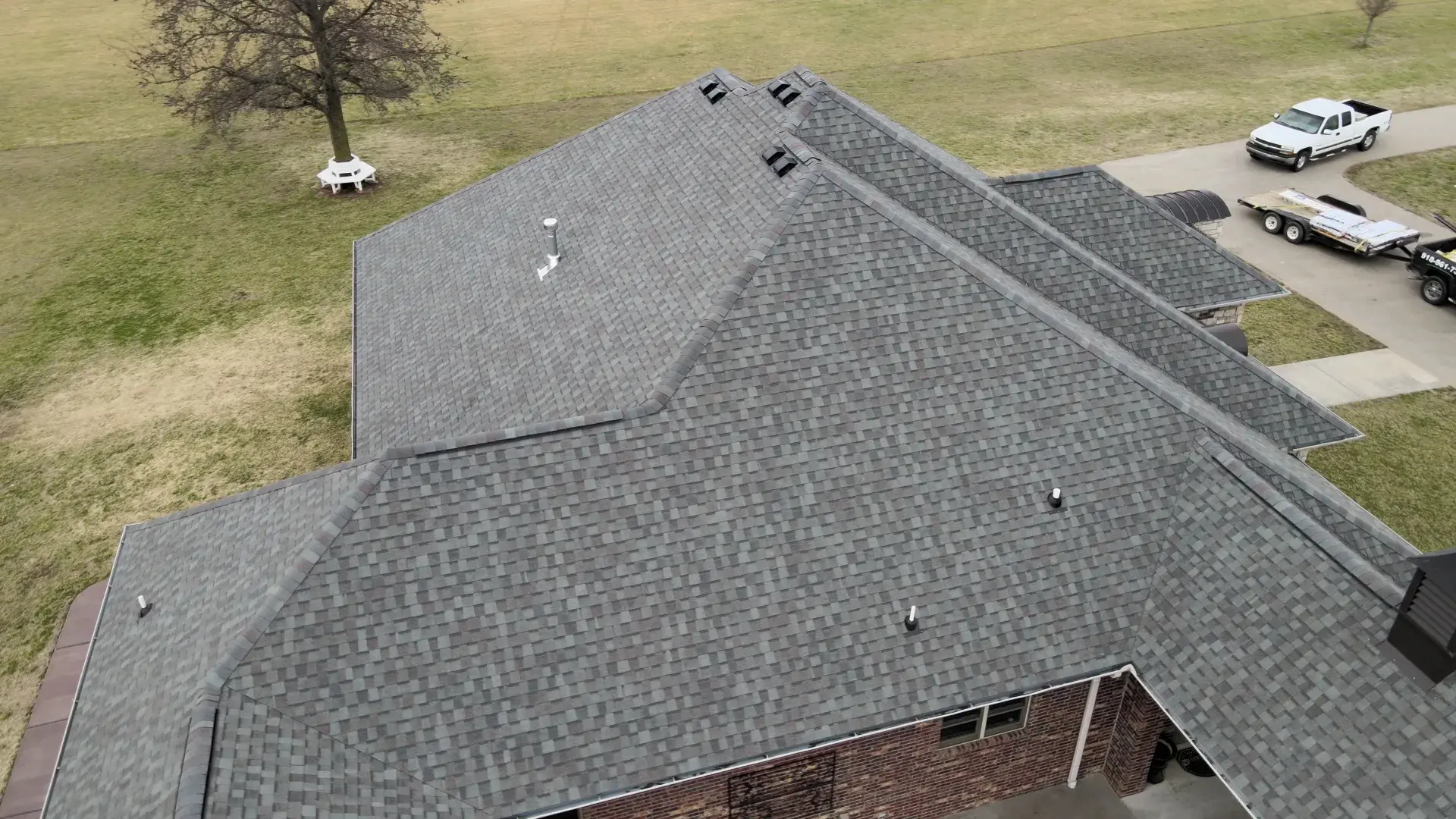 Aerial view of a newly completed charcoal shingle roof with multiple hips and valleys on a single-story brick home.