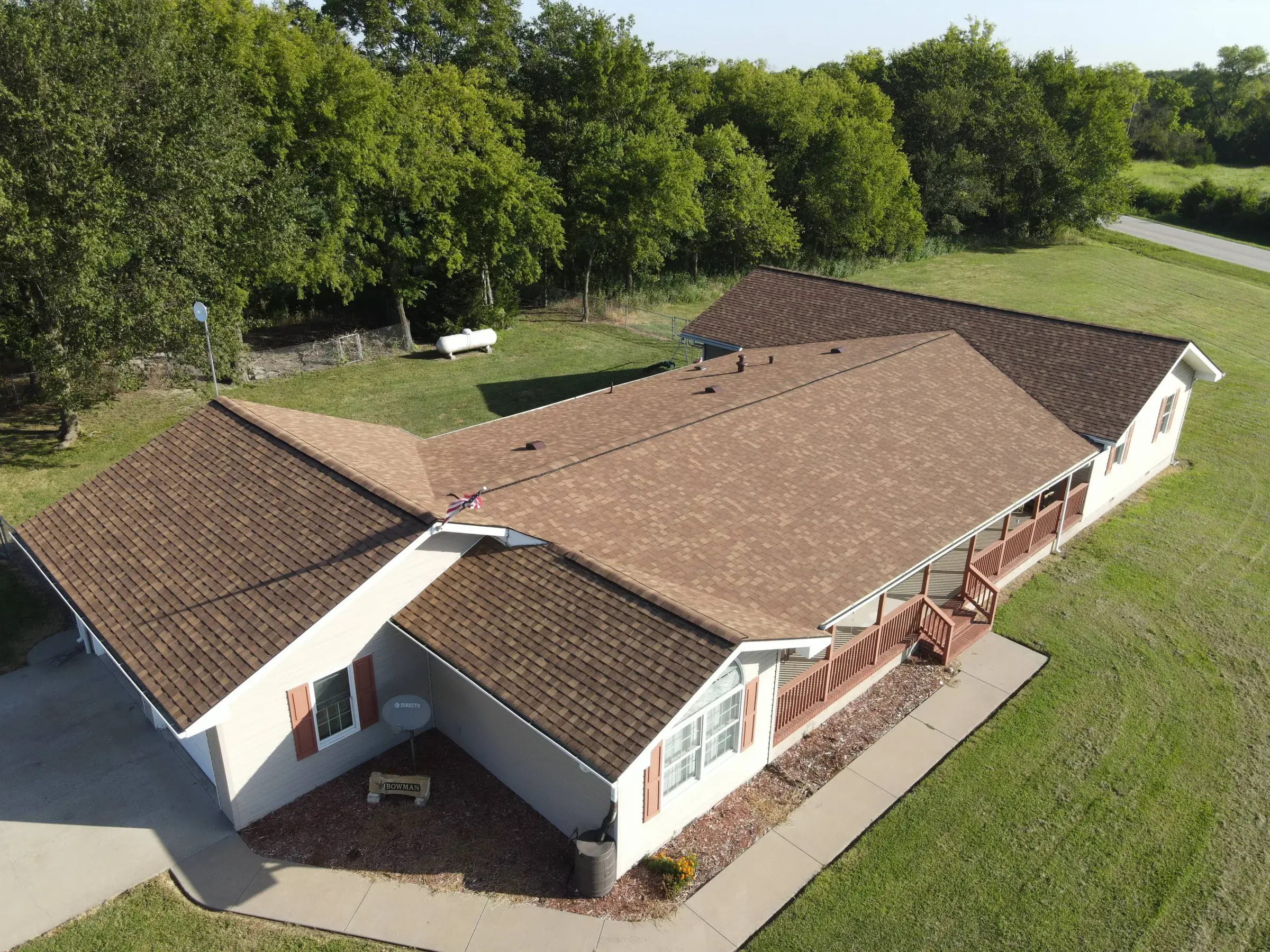 Aerial view of a ranch-style home with a new brown architectural shingle roof, white siding, and a covered front porch.