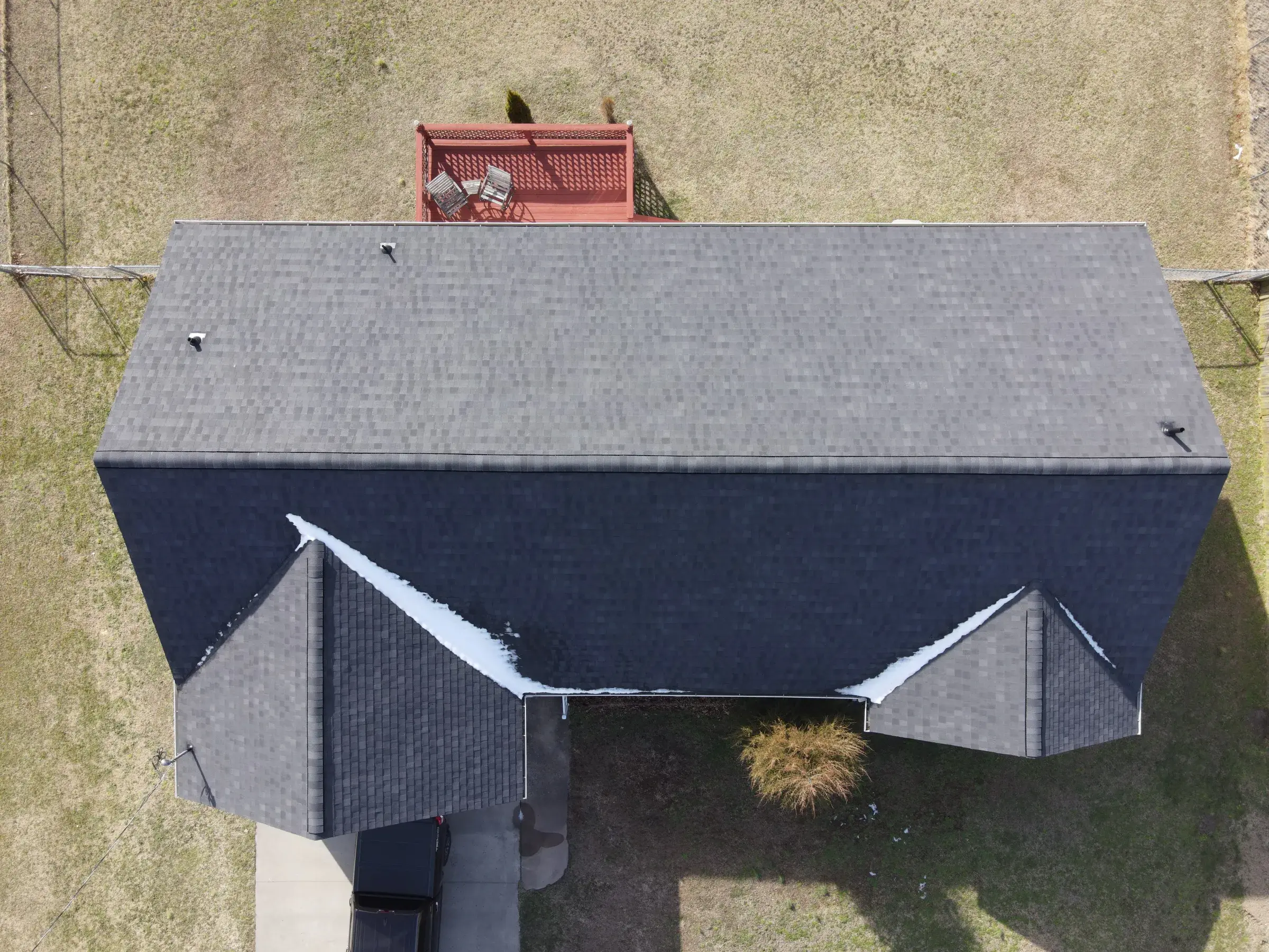Aerial view of a dark shingled roof with patches of snow remaining in the valleys and along a shaded gable.