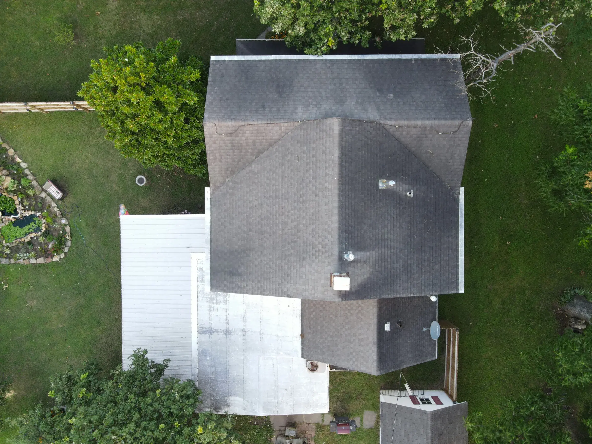 Overhead drone view of a house with a dark gray shingle roof next to a large white low-slope roof section.