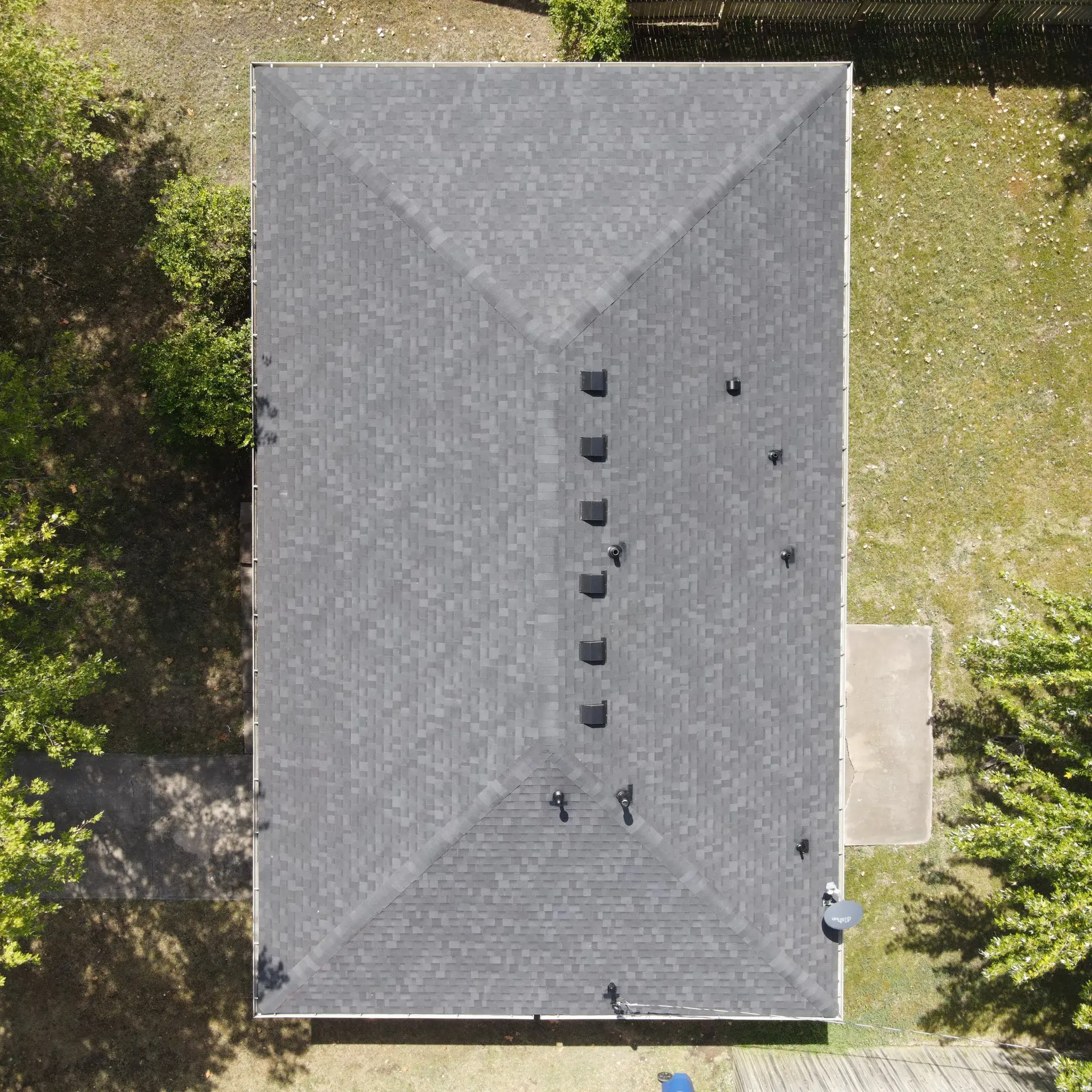Overhead drone view of a gray shingle hip roof with a row of six box vents running down the center.