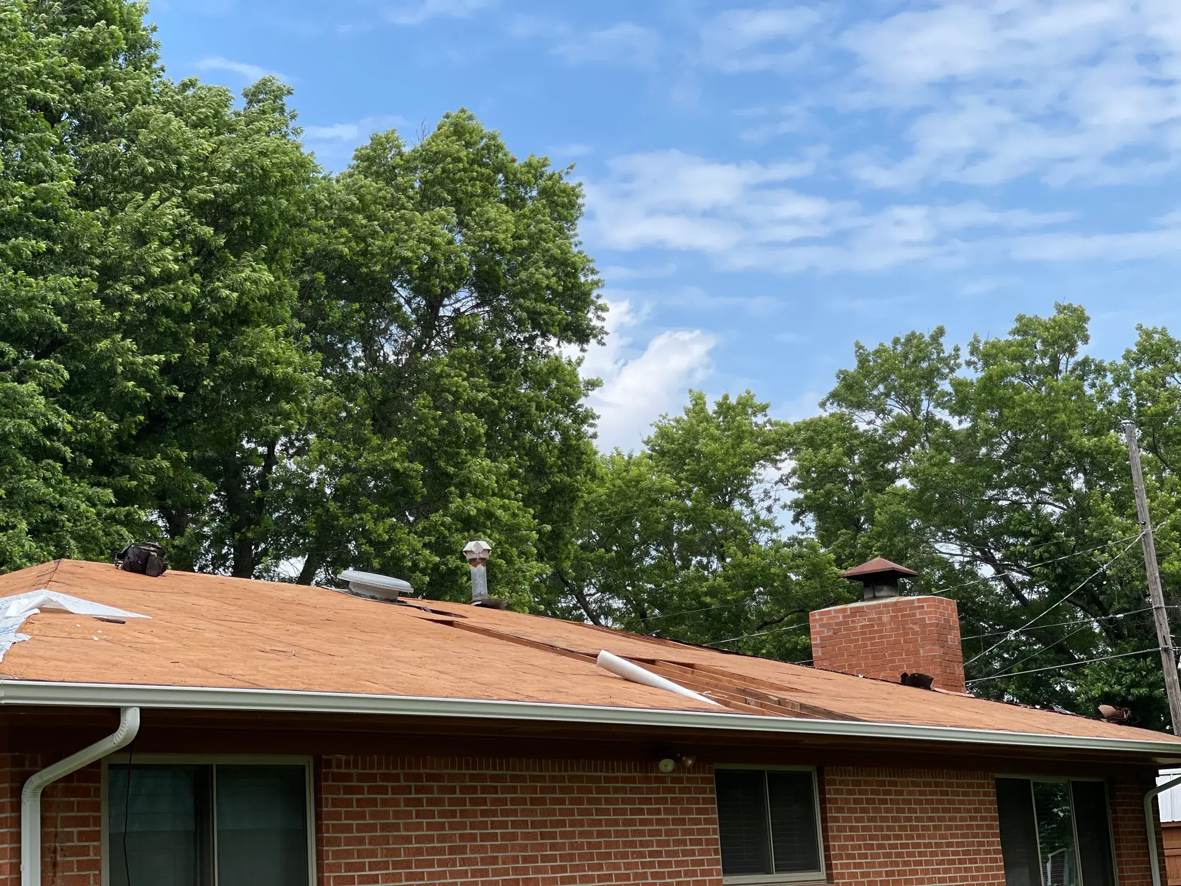 A brick house with its roof stripped to bare wood decking, with roof vents and a brick chimney still in place.